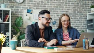 a man and a woman sitting at a table looking at a laptop by Vitaly Gariev courtesy of Unsplash.