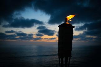 lighted tiki torch near sea at night by Kevin Finneran courtesy of Unsplash.