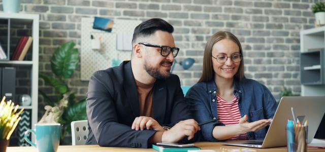 a man and a woman sitting at a table looking at a laptop by Vitaly Gariev courtesy of Unsplash.