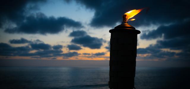 lighted tiki torch near sea at night by Kevin Finneran courtesy of Unsplash.